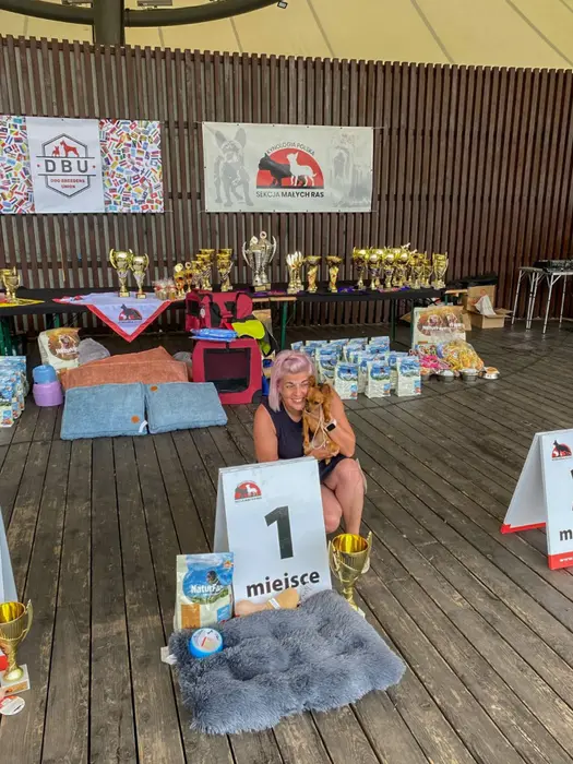 Expozantă cu câinele clasat pe locul întâi, lângă tăblița de premiere